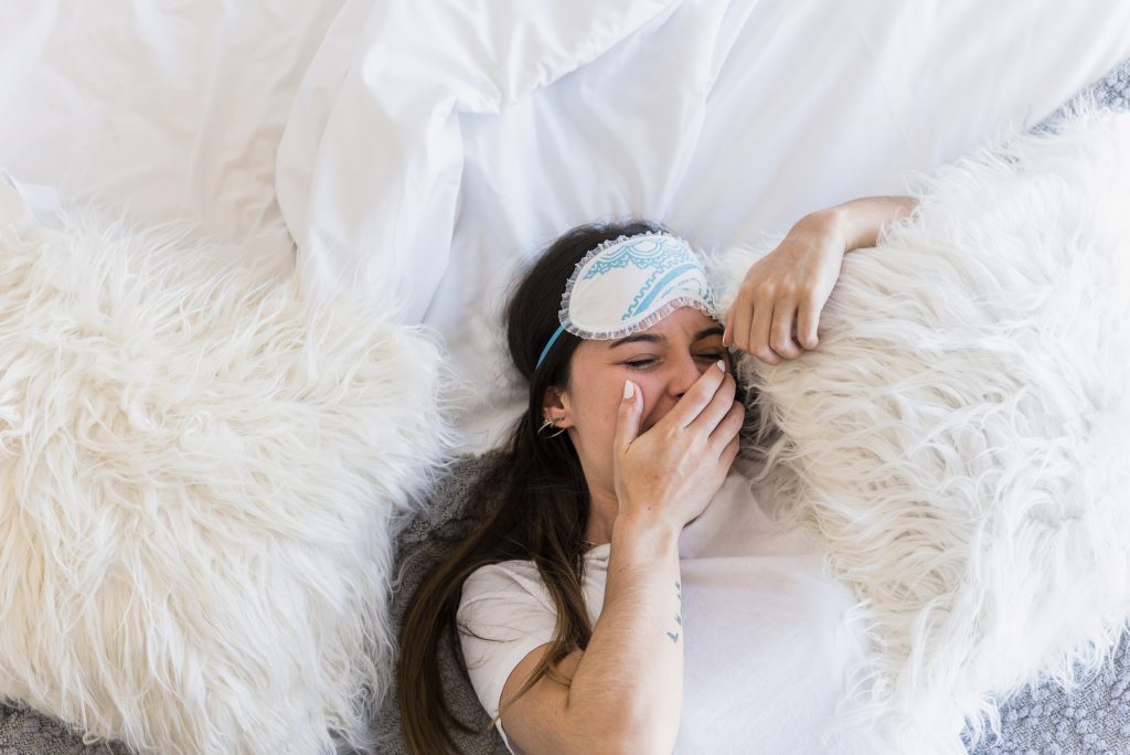 elevated view woman wearing eye mask lying bed yawning