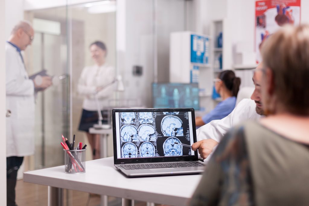 4 señales que no debemos ignorar: Cerebro en alerta: migraña, sueño, memoria y ACV. 1 senior woman hospital office looking brain ct scan while discussing with doctor about diagnosis sick young woman elderly medic with grey hair clinic corridor